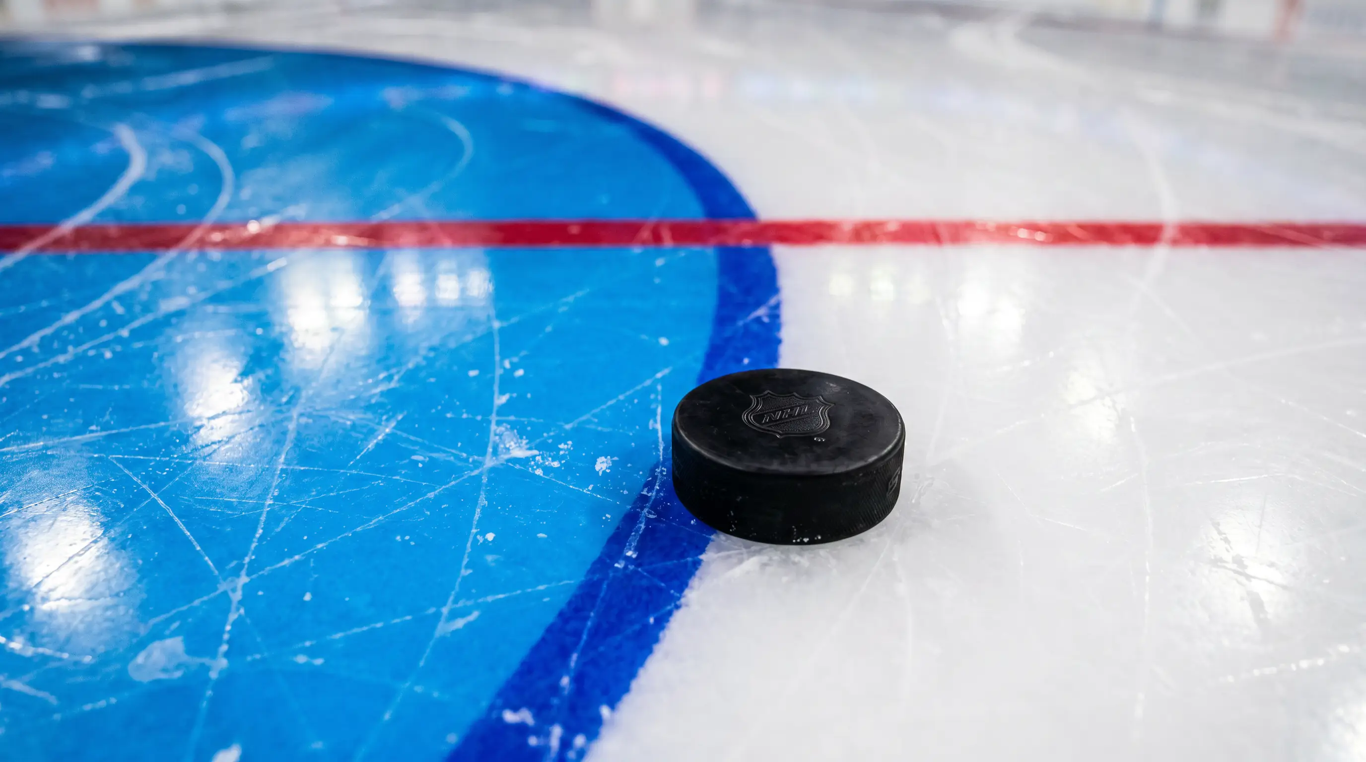 Close-up view of the blue painted goal crease and a hockey puck resting on the ice line