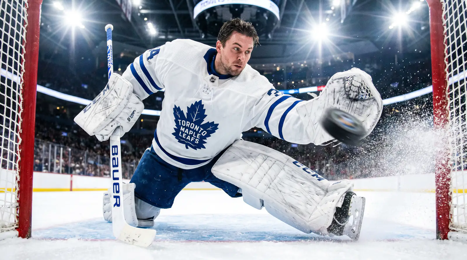 Ice hockey goalie diving across the crease as the puck slides toward goal